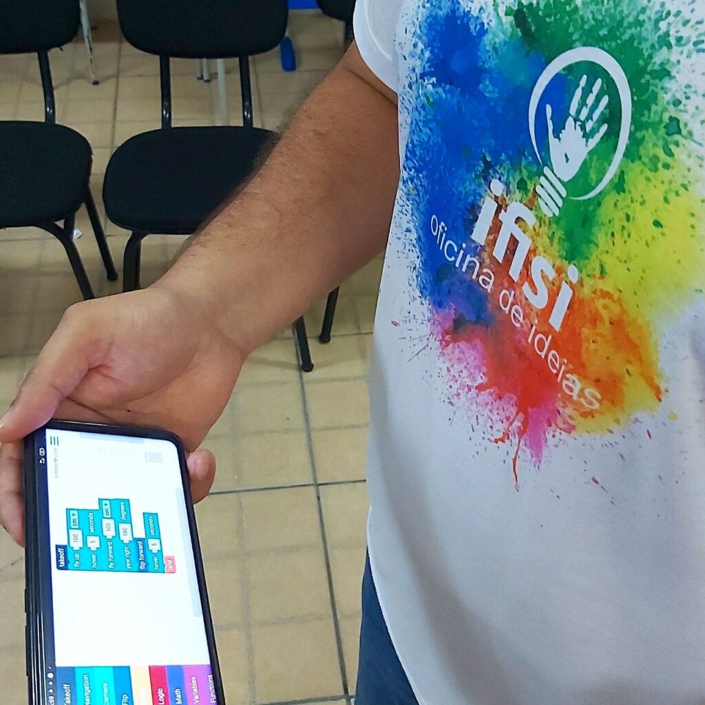 Imagem de um homem segurando um smartphone que na sua tela exibe um código feito com o droneblocks